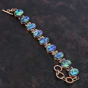 Könnte beinhalten: Ein Kupferarmband mit einem Kettenverschluss verfügt über ovale Einlagen aus Abalone-Muschel mit schillernden blauen, grünen und violetten Farbtönen.