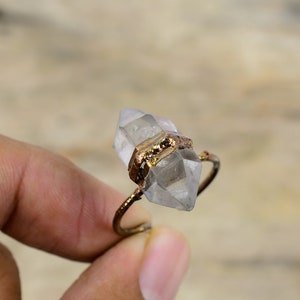 May include: A clear quartz crystal ring with a gold wire wrap. The ring is made of natural materials and has a unique, handcrafted look.