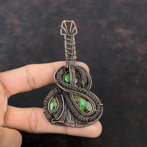 May include: A copper wire wrapped guitar pendant with green and purple gemstones. The pendant is shaped like a guitar with a detailed design.