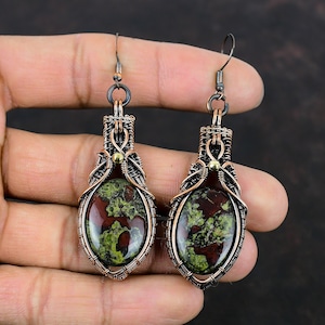 May include: A pair of copper wire wrapped earrings with green and red jasper stones. The earrings have a teardrop shape and are accented with gold wire.