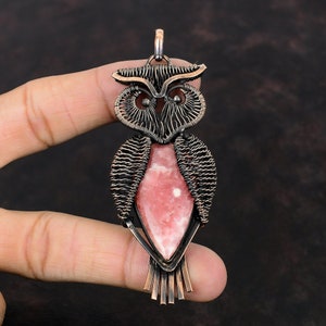 May include: A copper wire wrapped owl pendant with a pink and white gemstone in the center.