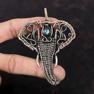 May include: A copper wire elephant pendant with a blue gemstone in the center. The pendant is intricately woven with wire and has a detailed design.