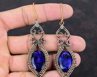 May include: A pair of copper wire wrapped earrings with a dark blue gemstone in the center of each earring. The earrings have a delicate, intricate design with a small gold accent at the top.