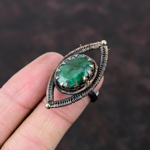 May include: A green gemstone ring with a copper and silver wire design. The ring is shaped like an eye.