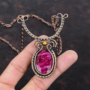 May include: A handcrafted copper wire necklace featuring a large, oval-shaped, magenta gemstone pendant. The pendant is intricately wire-wrapped and suspended from a delicate chain. The necklace has a unique, artistic design.