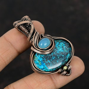 May include: A copper wire wrapped pendant featuring a blue and green gemstone with a smaller light blue gemstone set above it.