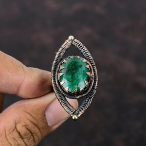 May include: A green gemstone ring with a copper wire setting. The ring is oval shaped and has a wire design that resembles an eye.