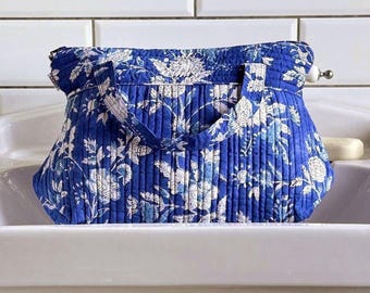 Op de afbeelding: Een blauwe gewatteerde tote bag met een bloemenpatroon in wit en lichtblauw. De tas heeft een rechthoekige vorm, een ritssluiting en twee handvatten. De tas ligt in een witte wastafel.