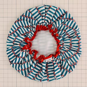 May include: A round shower cap with a white background, teal stripes, and red accents. The cap has a red ribbon drawstring and the word "caro" printed on the side.