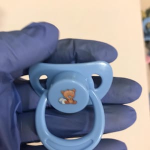 以下が含まれることがあります： 乳首に白いテディベアのデザインが施された薄い青色の哺乳瓶