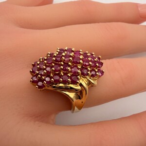 May include: A gold ring featuring a cluster of oval-cut rubies. The ring's band and setting are a polished gold color, and the rubies are a deep red hue. The ring is a statement piece of jewelry.
