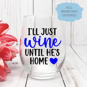 May include: A clear stemless wine glass with the text "I'll just wine until he's home" in black and blue. A blue heart is at the bottom. A large red flower is on the left side of the image.