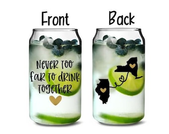 Pode incluir: Dois copos de vidro transparente em forma de lata com um gráfico preto e branco dos estados de Nova York e Illinois conectados por um coração. O copo da frente diz "Never too far to drink together" com um coração dourado.