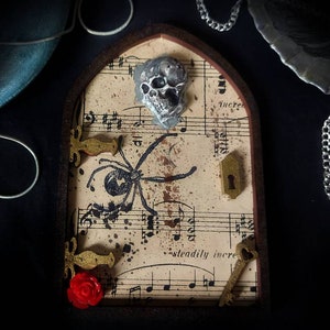 May include: A small, decorative door with a skull, spider, and musical notes on a beige background. The door has a gold keyhole and a gold key with a heart-shaped hole. There is a red rose on the bottom left corner of the door.