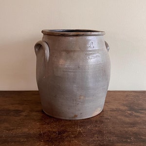 Puede incluir: Un tarro de gres gris con dos asas y un borde negro. El tarro tiene el número "21" y el texto "INTERNATIONAL STONEWARE CO.  CHICAGO" estampado en el lateral.