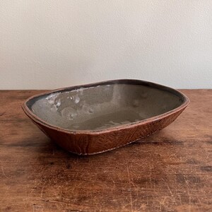 May include: A rectangular ceramic dish with a brown rim and a gray interior. The dish has a textured surface and is sitting on a wooden table.