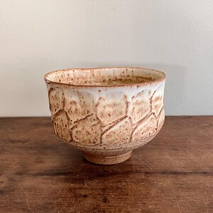 May include: A small, white ceramic bowl with a brown, textured pattern. The bowl has a rounded shape and a slightly flared rim.