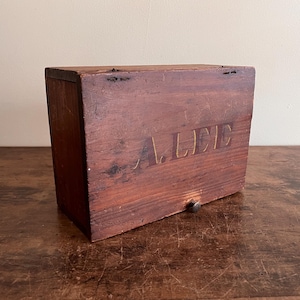 May include: A wooden box with a drawer and a metal knob. The box is painted brown and has the word "ALLIC" written on the front in gold paint.