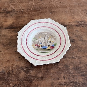 May include: A white ceramic plate with a scalloped edge and a red and white design. The centre of the plate features a colourful illustration of a group of people gathered around a man speaking. The text "FREE CHURCH" is visible at the bottom of the illustration.
