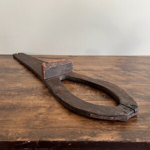 May include: A wooden shoe stretcher with a dark brown finish. The stretcher has a long handle and a horseshoe-shaped opening.