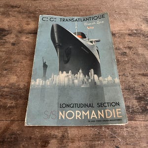 Puede incluir: Folleto vintage del S/S Normandie, un barco de la French Line. La portada presenta una ilustración estilizada del barco navegando por un paisaje urbano, con la Estatua de la Libertad visible. El texto incluye "Cie. Gen. Transatlantique" y "Longitudinal Section".