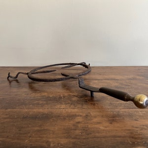 May include: A vintage cast iron and brass fireplace grate with a round shape and a long handle. The grate is rusty and has a worn finish.