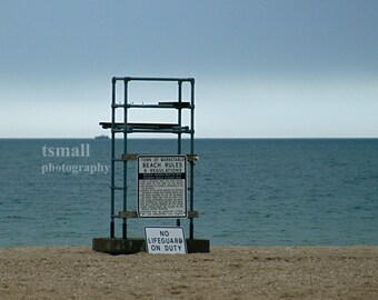 May include: A lifeguard stand on a sandy beach with the ocean in the background. The stand is made of metal pipes and has a sign that says "Town of Barnstable Beach Rules & Regulations" and another sign that says "No Lifeguard on Duty".