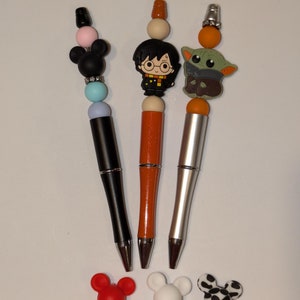 May include: Three pens with different character toppers. The first pen has a black Mickey Mouse topper, the second pen has a Harry Potter topper, and the third pen has a Baby Yoda topper.