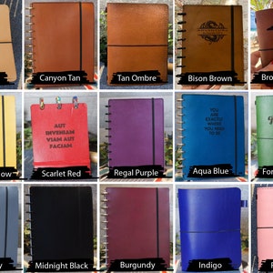 May include: A collection of 15 different colored leather-bound journals with various designs and text. The journals have a spiral binding and a black elastic band.
