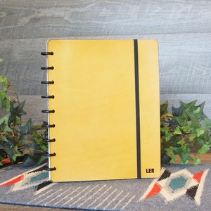 May include: A yellow leather bound notebook with a black elastic closure and a black coil binding. The notebook has the word "LER" printed on the bottom right corner.