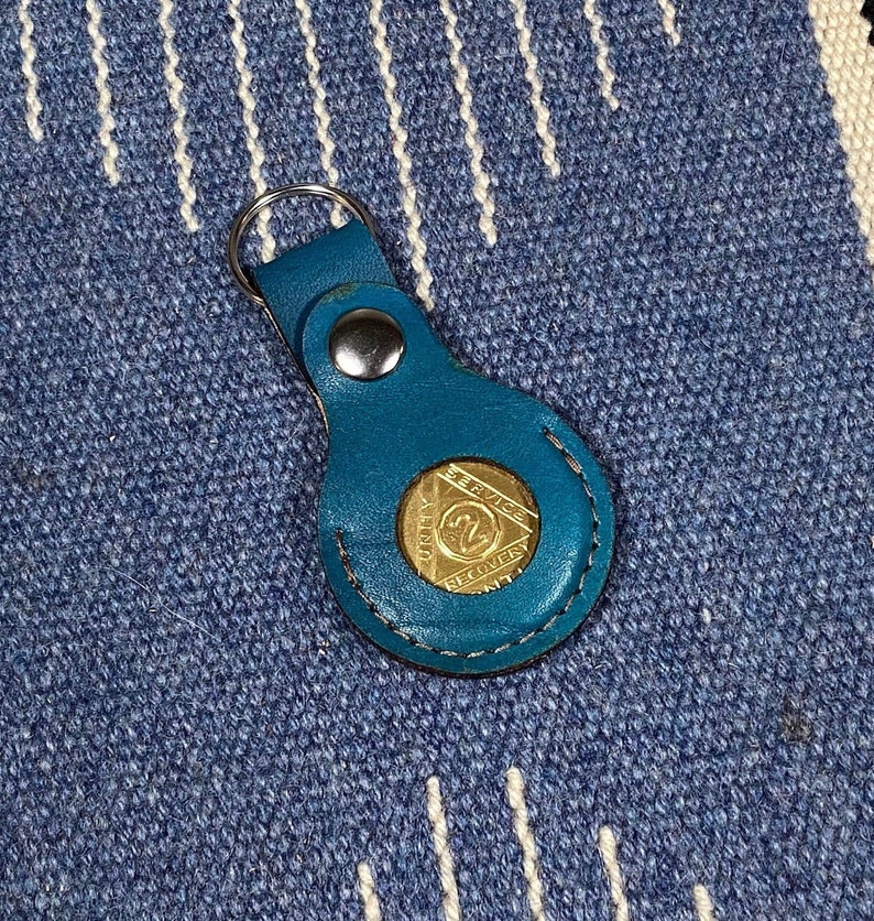 May include: A teal blue leather keychain with a gold metal coin featuring the text "20 Years Service and Recovery" and a number 20 inside a triangle.