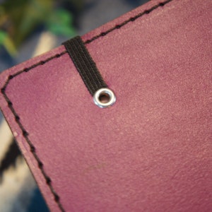 May include: Close-up of a purple leather notebook with a black elastic band and a silver metal eyelet.