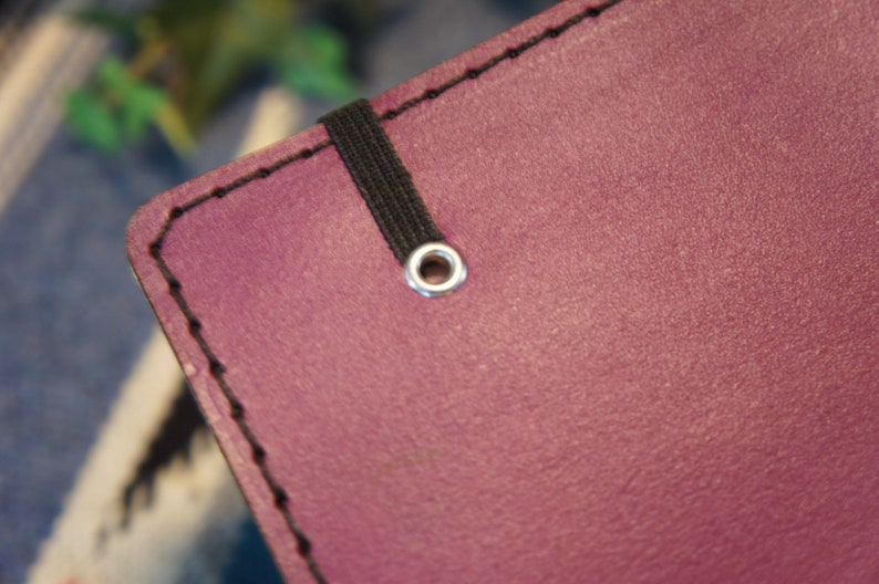May include: Close-up of a purple leather notebook with a black elastic band and a silver metal eyelet.