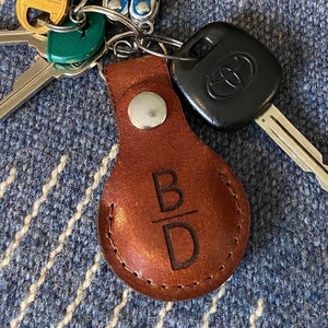 May include: A brown leather keychain with the initials "B/D" engraved on it. The keychain is attached to a silver key ring with a car key.