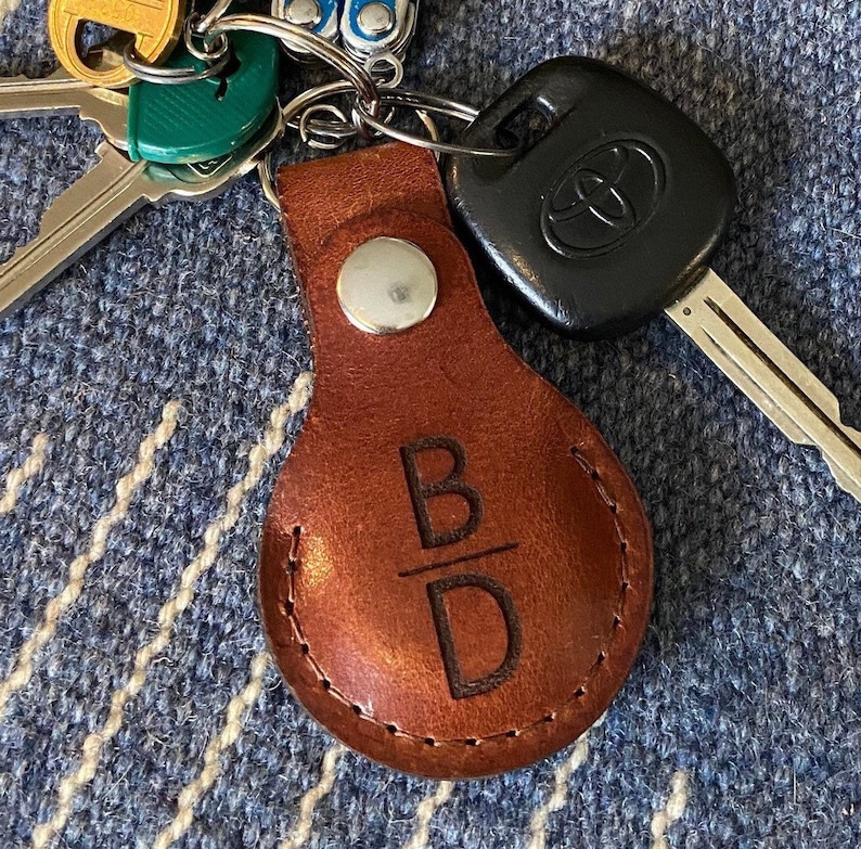 May include: A brown leather keychain with the initials "B/D" engraved on it. The keychain is attached to a silver key ring with a car key.