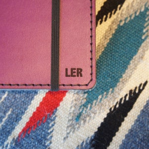 May include: A close-up of a purple leather notebook with a black elastic band and the initials "LER" embossed on the cover.