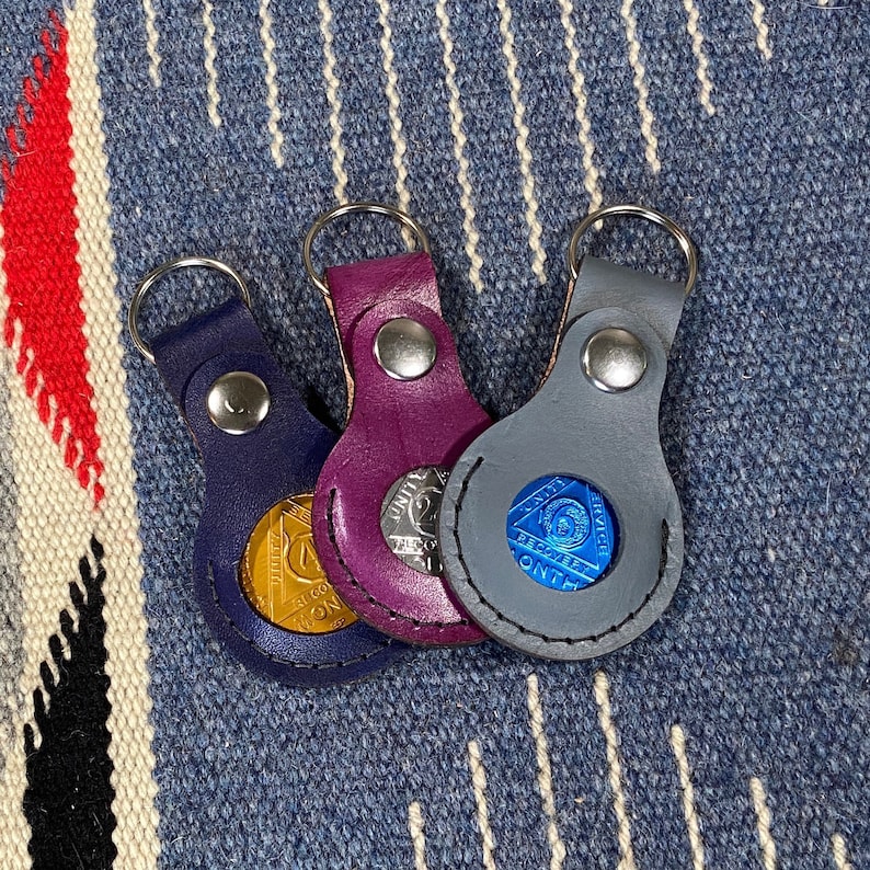 May include: Three leather keychains with different colored leather and metal coin inserts. The coins have the words "United States" and "Service" on them. The coins are different colors, gold, blue, and silver.