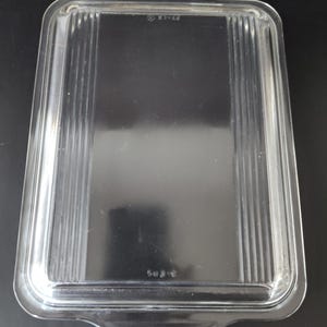 Könnte beinhalten: Ein klarer, rechteckiger Pyrex-Glasdeckel mit vertikalen Rillen. Der Deckel hat abgerundete Ecken und zwei kleine Griffe. Der Text "X1-22" und "503-C" ist sichtbar.