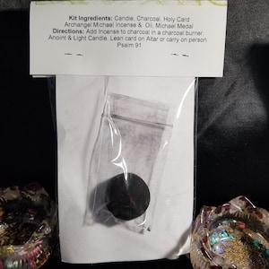 May include: A white card with the text "Kit Ingredients: Candle, Charcoal, Holy Card Archangel Michael Incense & Oil, Michael Medal Directions: Add Incense to charcoal in a charcoal burner. Anoint & Light Candle. Lean card on Altar or carry on person. Psalm 91" and a small black charcoal disc in a clear plastic bag.