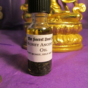 Peut inclure: Une petite bouteille en verre avec un bouchon noir remplie d'un liquide clair et d'herbes vertes. La bouteille porte une &eacute;tiquette blanche avec le texte "The Secret Door Money Anoint Oil" et "Attract Money, Self And Abundance".