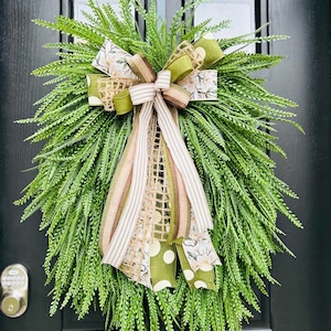 May include: A green wreath with a large bow made of brown, white, and green ribbon. The bow has a burlap texture and a floral pattern.