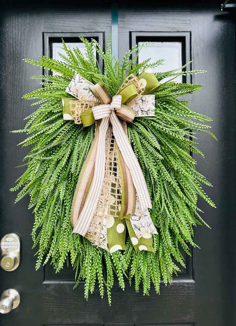 May include: A green wreath with a large bow made of brown, white, and green ribbon. The bow has a burlap texture and a floral pattern.