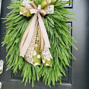 May include: A green wreath with a brown and white striped ribbon, a green polka dot ribbon, and a brown and green burlap ribbon. The wreath is hanging on a black door.