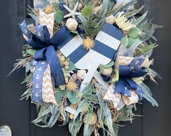 May include: A nautical themed wreath with blue and white striped wooden paddles, blue and white anchor ribbon, and greenery.