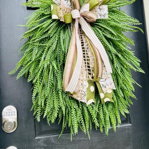 May include: A green fern wreath with a large bow made of brown, white, and green ribbon. The bow has a floral pattern and white polka dots.
