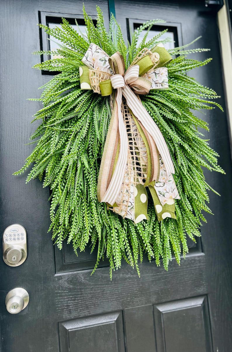 May include: A green fern wreath with a large bow made of brown, white, and green ribbon. The bow has a floral pattern and white polka dots.