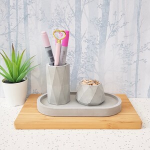 May include: A grey concrete desk organiser set with a pen holder, a small bowl for paper clips, and a tray. The set is on a wooden surface.