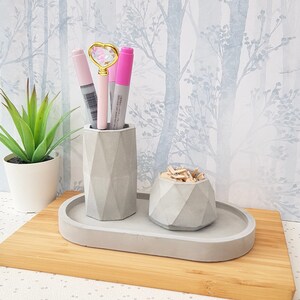 May include: A grey concrete desk organiser set with an oval tray, a pencil holder, and a small bowl. The set is on a wooden surface.