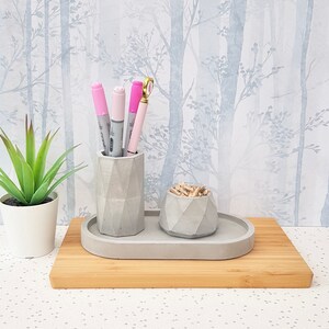 May include: A grey concrete desk organiser set with a pen holder and a small bowl for paper clips. The set is on a wooden tray and has a geometric design.