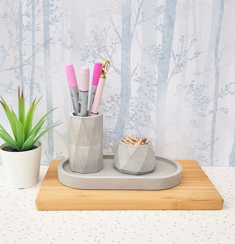 May include: A grey concrete desk organiser set with a pen holder and a small bowl for paper clips. The set is on a wooden tray and has a geometric design.